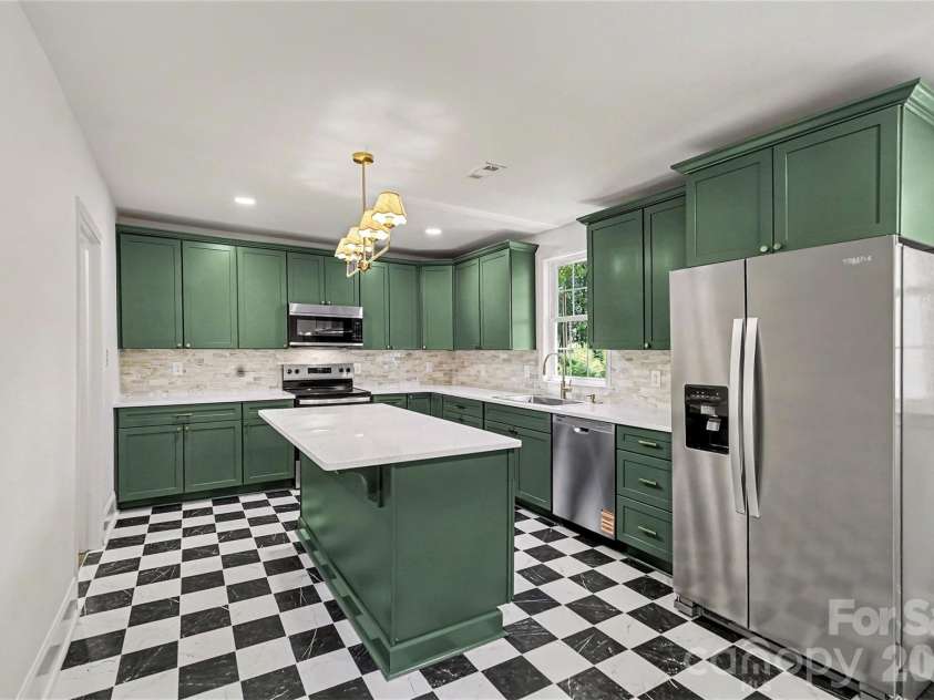 601 Marion Sims Drive, Lancaster, SC 29720.  MLS# CAR4404710, YatesRealty ID 48048. Sunlit kitchen featuring statement black-and-white tiled floors, warm gold fixtures, stainless steel refrigerator, and direct sight lines to the surrounding greenery and main dining/living room.
