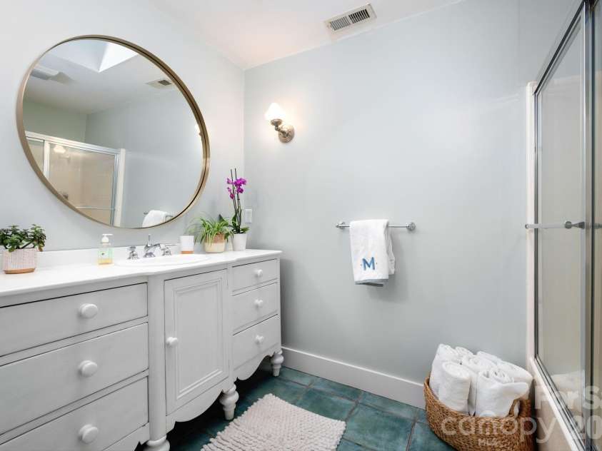 183 Blarney Road, Lake Lure, NC 28746.  MLS# CAR4326369, YatesRealty ID 49285. Main level bathroom has ceramic tile, skylight, bath, shower combo, and large vintage painted vanity
