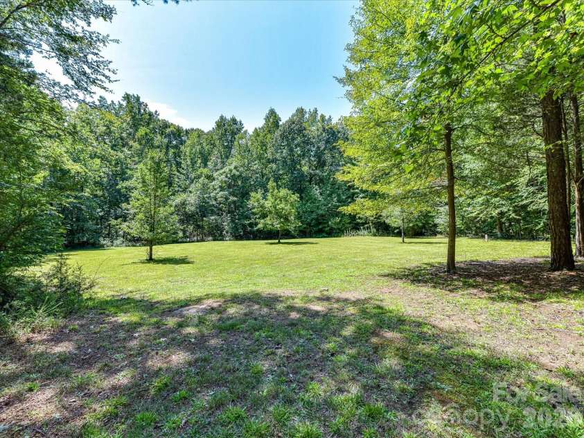 9821 Harvest Lane, Davidson, NC 28036.  MLS# CAR4422485, YatesRealty ID 49465. Expansive backyard offers a large open lawn surrounded by mature trees, creating a peaceful and private outdoor setting.