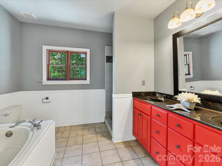 9821 Harvest Lane, Davidson, NC 28036.  MLS# CAR4422485, YatesRealty ID 49465. Primary bath features tile flooring, a soaking tub, separate shower, spacious vanity, and natural light from a wooded-view window.