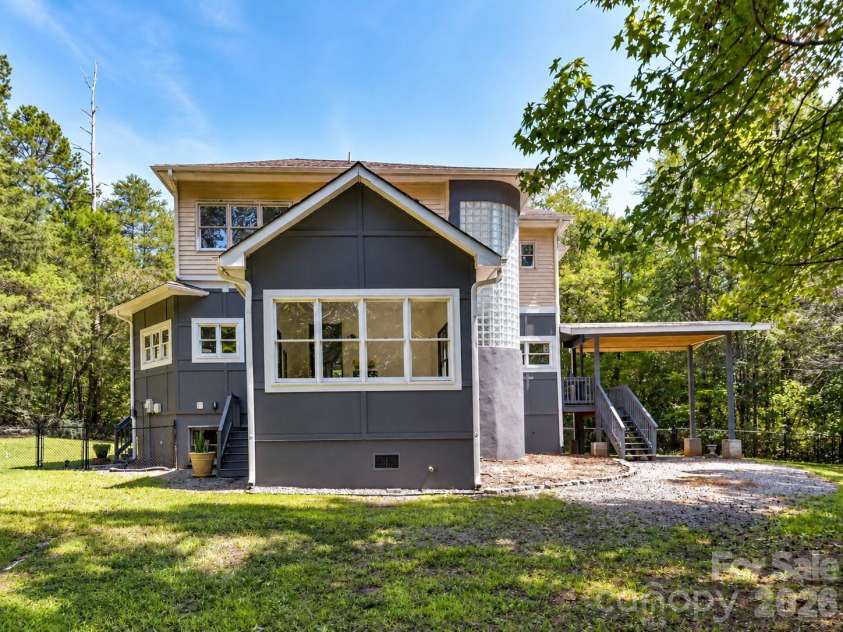 9821 Harvest Lane, Davidson, NC 28036.  MLS# CAR4422485, YatesRealty ID 49465. Rear view highlights the home’s distinctive architecture, expansive windows, covered outdoor living space, and private wooded backdrop.