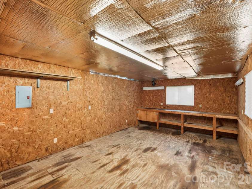 168 Country Lane, Mills River, NC 28759.  MLS# CAR4422309, YatesRealty ID 49874. Spacious outbuilding interior with workbench, lighting, electrical panel, and plenty of room for projects or storage.