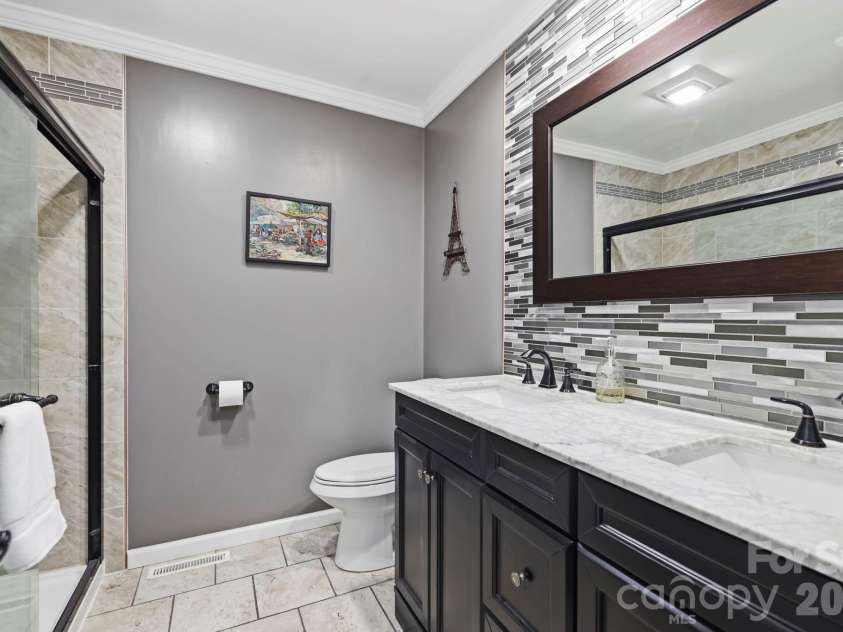 168 Country Lane, Mills River, NC 28759.  MLS# CAR4422309, YatesRealty ID 49874. Updated full bath features a double-sink vanity, tiled shower, stylish backsplash, and coordinated modern finishes.