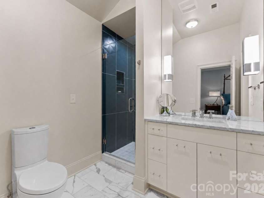 974 Queens Road, Charlotte, NC 28207.  MLS# CAR4413389, YatesRealty ID 50053. A sleek, contemporary bath features marble flooring, a streamlined marble-topped vanity with ample storage, and a striking glass-enclosed shower with dramatic dark tile—an elegant complement to the adjoining bedroom.