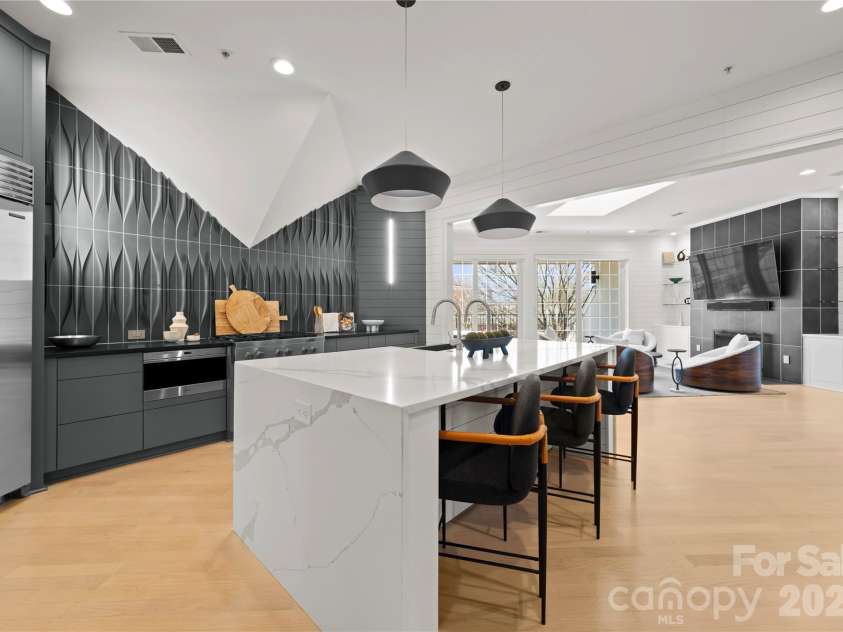974 Queens Road, Charlotte, NC 28207.  MLS# CAR4413389, YatesRealty ID 50053. Contemporary Chef’s Kitchen — A dramatic waterfall island with seating, matte dark cabinetry, sculptural tile backsplash and oversized pendant lights create a sleek professional kitchen that opens seamlessly to the family 