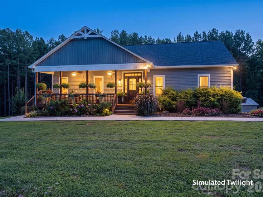 1551 Brevard Place Road, Iron Station, NC 28080.  MLS# CAR4422440, YatesRealty ID 50132. Simulated twilight view showcasing the inviting covered front porch, beautiful landscaping, and peaceful wooded setting.