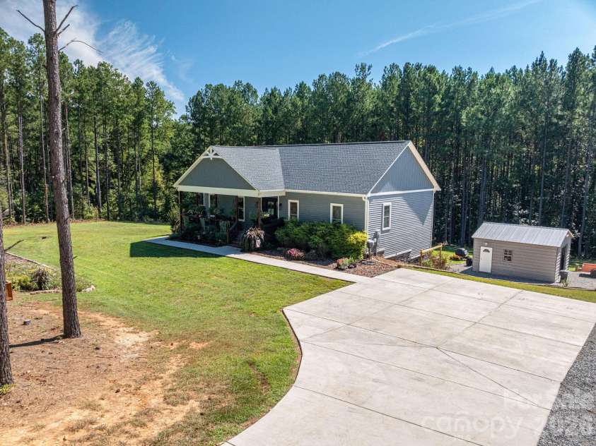 1551 Brevard Place Road, Iron Station, NC 28080.  MLS# CAR4422440, YatesRealty ID 50132. Spacious concrete parking area, sidewalk access, detached workshop, and wooded surrounds.