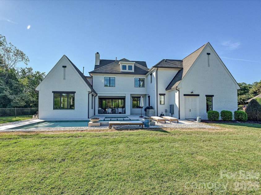 18717 Square Sail Road, Cornelius, NC 28031.  MLS# CAR4424933, YatesRealty ID 51420. Rear exterior highlights the home’s striking architecture, expansive lawn, covered patio, and seamless connection to the private pool and outdoor living areas.