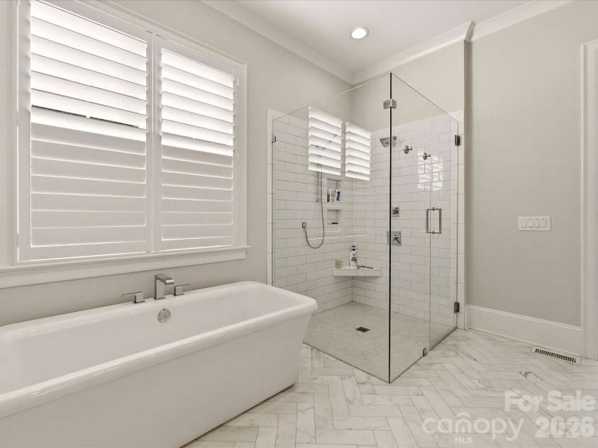 18717 Square Sail Road, Cornelius, NC 28031.  MLS# CAR4424933, YatesRealty ID 51420. Spa-inspired Primary Bath features a freestanding soaking tub, oversized frameless glass shower, dual vanities with stone countertops, and elegant herringbone-patterned tile flooring.