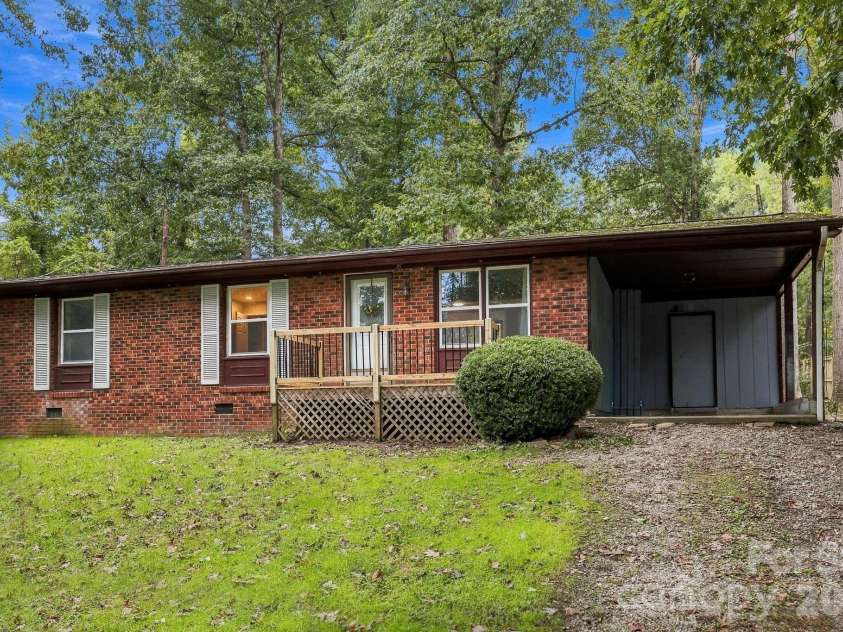 36 Medlin Lane, Flat Rock, NC 28731.  MLS# CAR4428597, YatesRealty ID 53594. Another exterior angle highlighting the home’s brick front, front entry deck, and attached carport.