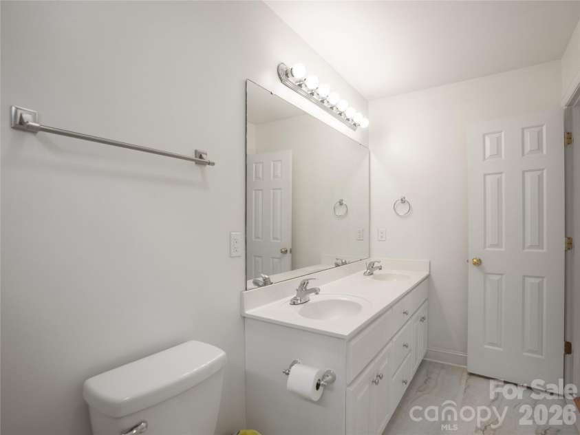 1011 Overhill Drive, Salisbury, NC 28144.  MLS# CAR4429292, YatesRealty ID 54283. Bright secondary bathroom featuring a dual-sink vanity, expansive vanity mirror with multi-bulb lighting, white cabinetry, and updated flooring.