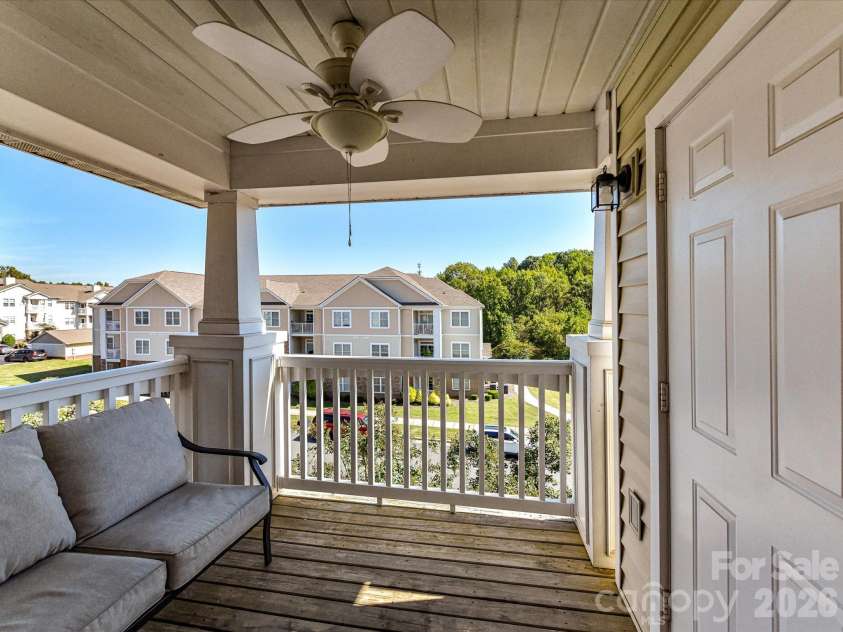 9031 Mcdowell Creek Court, Cornelius, NC 28031.  MLS# CAR4428404, YatesRealty ID 54302. Covered balcony featuring a ceiling fan, outdoor seating, and an elevated view overlooking the surrounding community and mature greenery.