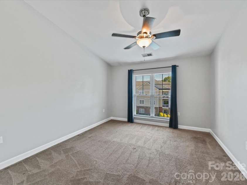 9031 Mcdowell Creek Court, Cornelius, NC 28031.  MLS# CAR4428404, YatesRealty ID 54302. Spacious primary suite featuring plush carpeting, a ceiling fan, and a large window providing abundant natural light and elevated community views.