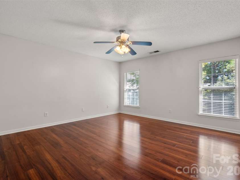 2738 Mill Valley Court, Matthews, NC 28105.  MLS# CAR4424420, YatesRealty ID 54340. Expansive upper-level primary bedroom featuring rich laminate flooring, ceiling fan with light fixture, and multiple windows for abundant natural light.