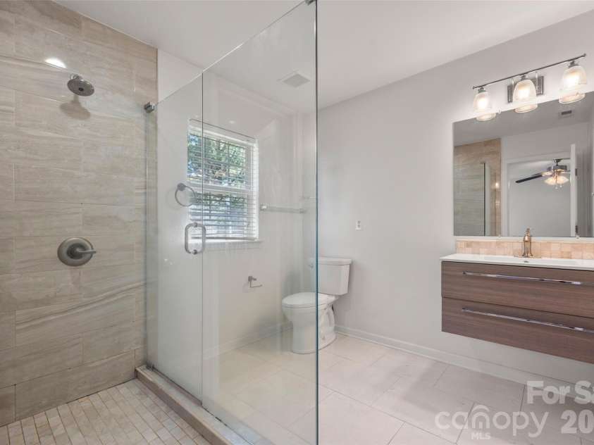 2738 Mill Valley Court, Matthews, NC 28105.  MLS# CAR4424420, YatesRealty ID 54340. Upgraded primary en-suite bathroom featuring a modern floating vanity with under-cabinet lighting, updated mirror and vanity light, tile flooring, and a large walk-in glass shower.