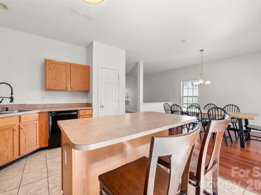 2738 Mill Valley Court, Matthews, NC 28105.  MLS# CAR4424420, YatesRealty ID 54340. View from behind the kitchen island toward the dining area, featuring double sinks, modern gooseneck faucet, dishwasher, and tile flooring.