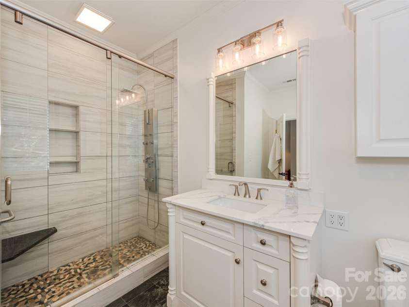 723 Romany Road, Charlotte, NC 28203.  MLS# CAR4430250, YatesRealty ID 55141. The en-suite primary bath pairs style with function, featuring a spacious shower with a built-in bench, a beautiful vanity, and a coordinating armoire that provides additional storage.