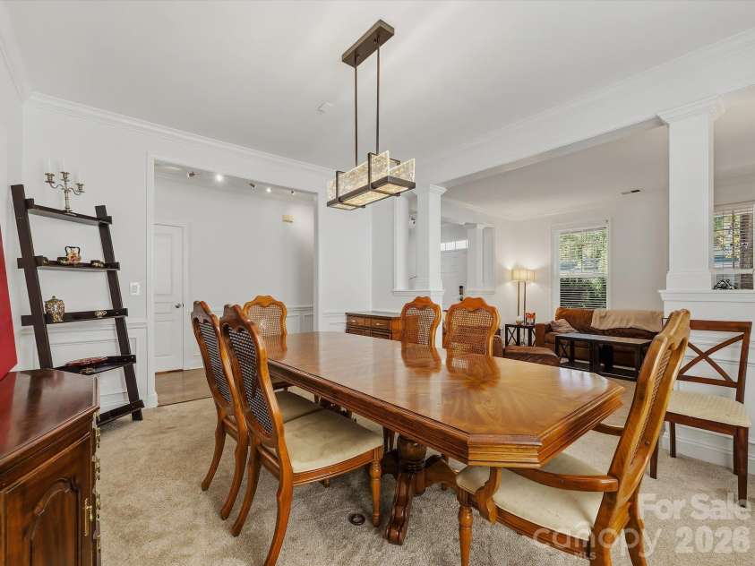 11732 Windy Mist Way, Huntersville, NC 28078.  MLS# CAR4431912, YatesRealty ID 55502. A spacious formal dining room features elegant crown molding, architectural columns, and a contemporary statement light fixture, creating an inviting setting for gatherings and entertaining.