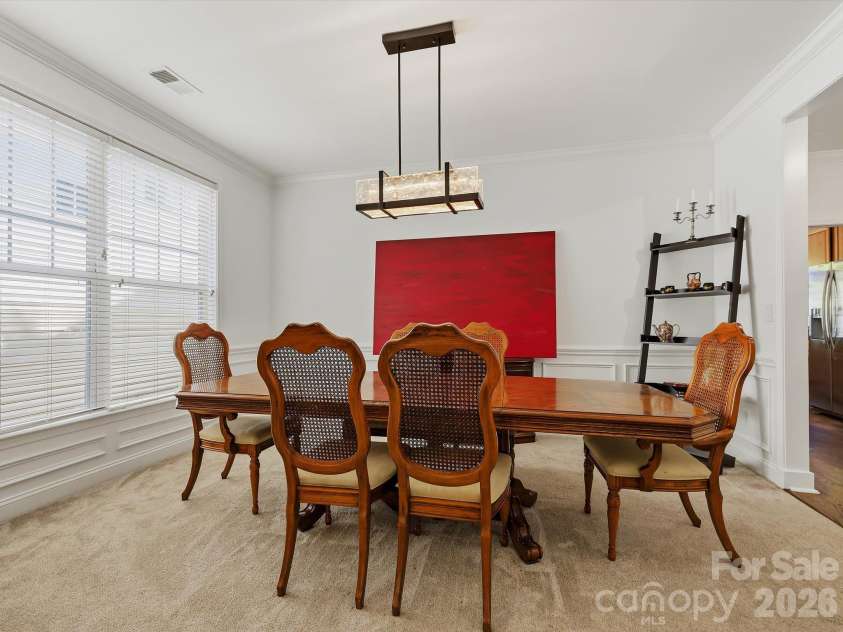 11732 Windy Mist Way, Huntersville, NC 28078.  MLS# CAR4431912, YatesRealty ID 55502. A spacious formal dining room features elegant crown molding, architectural columns, and a contemporary statement light fixture, creating an inviting setting for gatherings and entertaining.