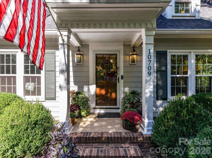 10709 Danesway Lane, Cornelius, NC 28031.  MLS# CAR4431451, YatesRealty ID 55685. The charming covered front porch features classic white columns, elegant lantern lighting, a welcoming entryway, and beautifully manicured landscaping with colorful seasonal flowers.
