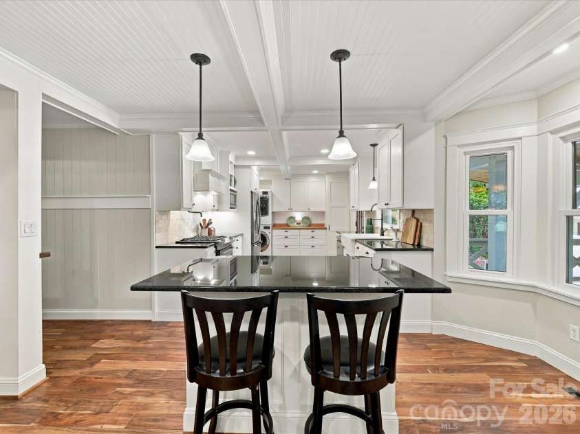 10709 Danesway Lane, Cornelius, NC 28031.  MLS# CAR4431451, YatesRealty ID 55685. The inviting dining area features a spacious breakfast bar with seating, elegant pendant lighting, rich hardwood floors, and beautiful coffered ceilings, seamlessly connecting to the chef's kitchen.