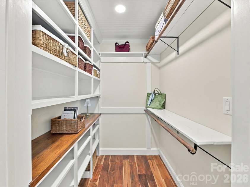 10709 Danesway Lane, Cornelius, NC 28031.  MLS# CAR4431451, YatesRealty ID 55685. The spacious Primary Closet features custom built-in shelving, multiple hanging rods, convenient storage compartments, warm wood countertops, and rich hardwood floors for exceptional organization and functionality.