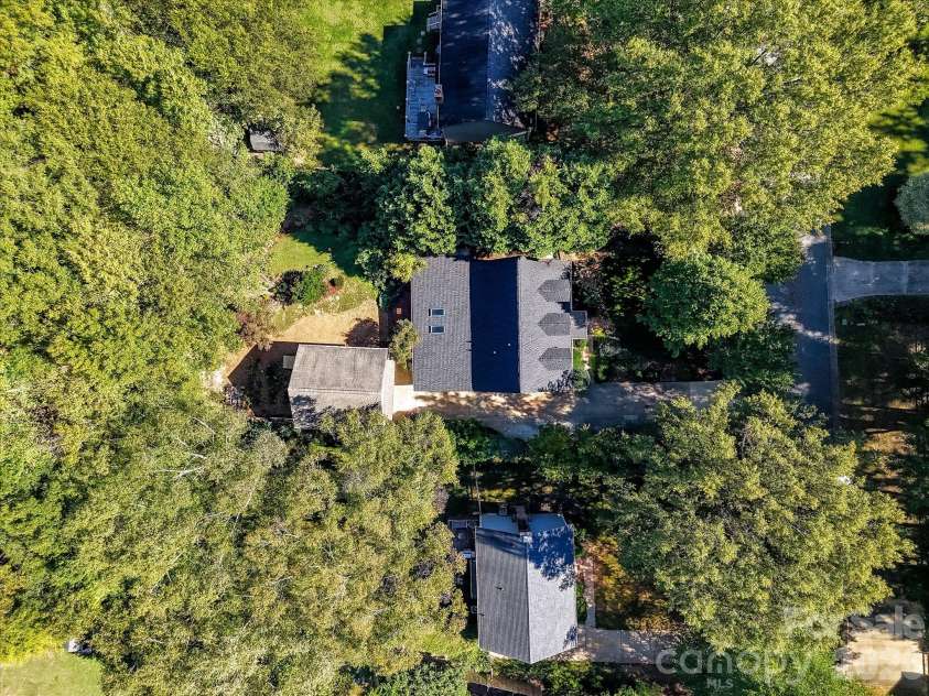 10709 Danesway Lane, Cornelius, NC 28031.  MLS# CAR4431451, YatesRealty ID 55685. This stunning aerial view showcases the home's private, tree-lined setting, surrounded by mature trees and lush greenery, with a detached two-car garage, spacious driveway, and beautifully landscaped backyard.