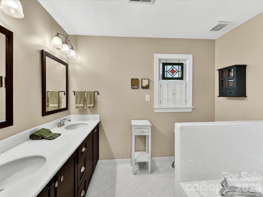 207 Hobbs Street, Davidson, NC 28036.  MLS# CAR4359786, YatesRealty ID 5932. Spacious primary bathroom featuring a dual-sink vanity, ample counter space, and a soaking tub, all accented by charming details and natural light.