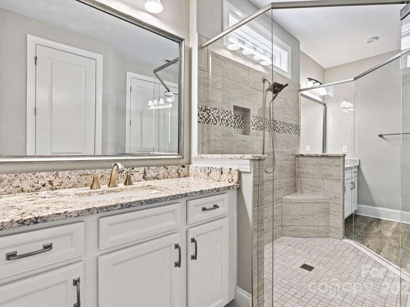 8718 Festival Way, Charlotte, NC 28215.  MLS# CAR4243722, YatesRealty ID 6122. A transom window above the tiled shower with frameless surround, fills the space with natural light, highlighting the elegant tile floors.