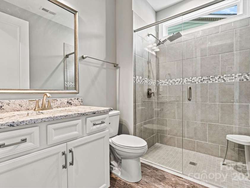 8718 Festival Way, Charlotte, NC 28215.  MLS# CAR4243722, YatesRealty ID 6122. The guest bath has tile flooring, walk-in tiled frameless shower w/ shampoo niche, elegant cabinetry, sleek granite countertop and framed mirror. A transom window above the shower allows abundant natural light.