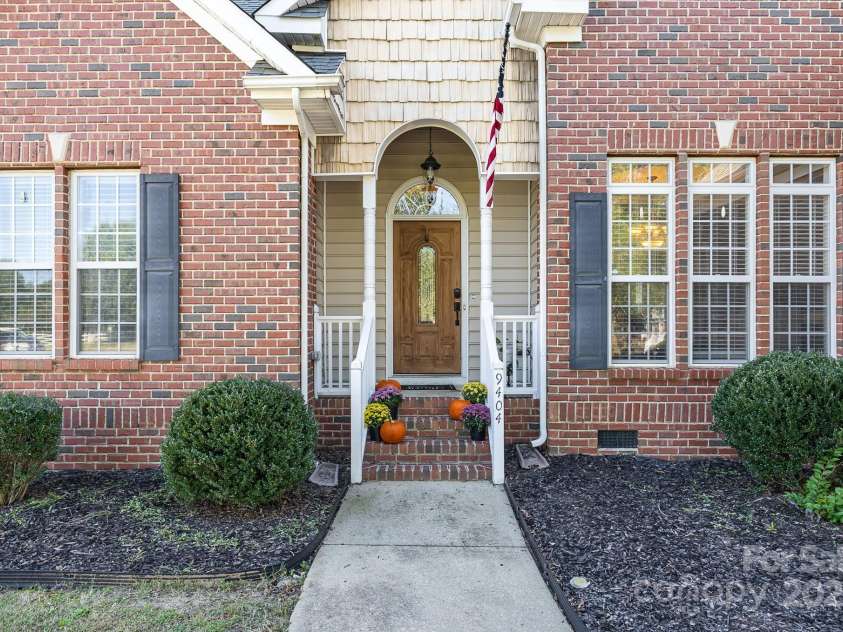 9404 Perimeter Court, Zebulon, NC 27597.  MLS# CAR4191333, YatesRealty ID 6842. The covered front entrance of this charming brick home showcases a stunning wooden door with elegant accents, offering a warm and inviting welcome.