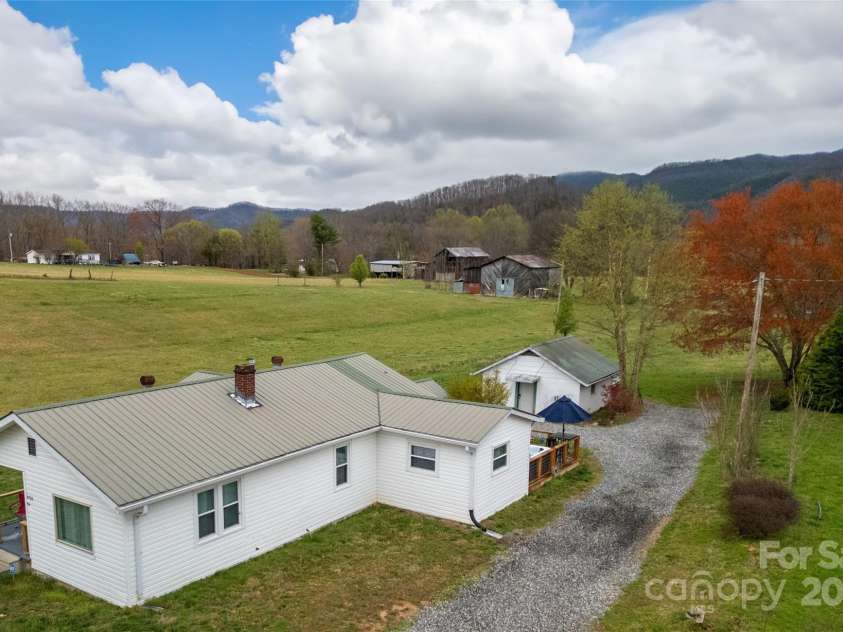 626 Fairview Loop, Hot Springs, NC 28743.  MLS# CAR4302454, YatesRealty ID 706. House Side from above street. Red Maple and Birch Trees in Spring. Meadow, Barns and Mountains beyond. 