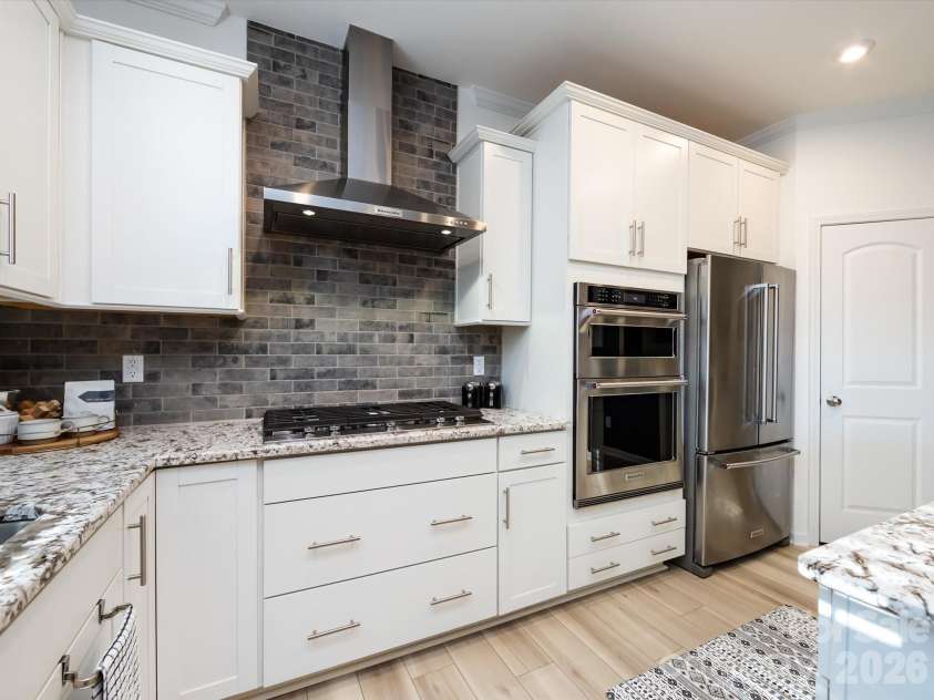 8903 Ansley Park Place, Huntersville, NC 28078.  MLS# CAR4366272, YatesRealty ID 8920. Alternate view of the kitchen showcasing granite countertops, gas cooktop with vent hood, stainless steel appliances, and crisp white cabinetry with stylish backsplash.