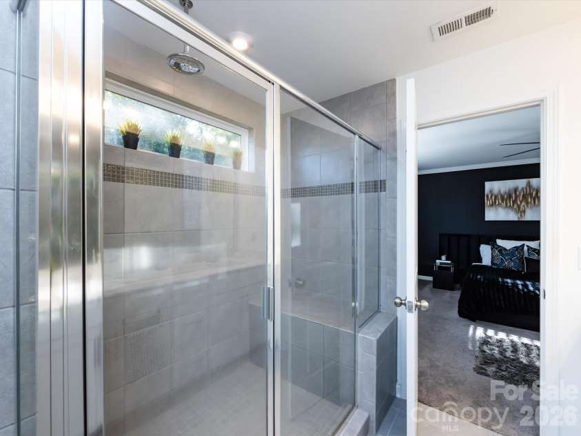 8903 Ansley Park Place, Huntersville, NC 28078.  MLS# CAR4366272, YatesRealty ID 8920. Elegant primary shower featuring floor-to-ceiling tile, glass enclosure, and built-in bench with natural light from a transom window.