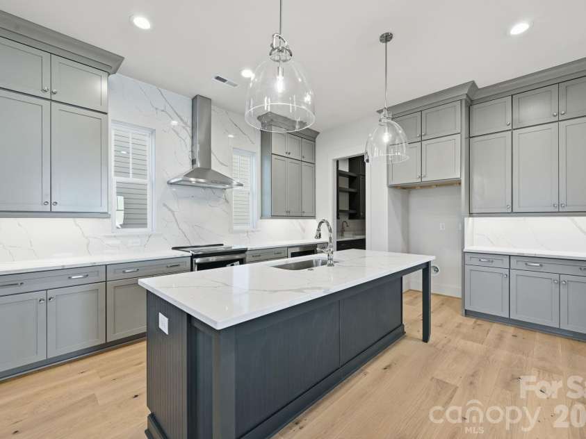 7245 Westrow Avenue, Charlotte, NC 28278.  MLS# CAR4314661, YatesRealty ID 982. Designer kitchen showcasing a spacious center island, stacked cabinetry extending to the ceiling for a custom-built look, and a sleek quartz backsplash that adds sophistication and easy maintenance.