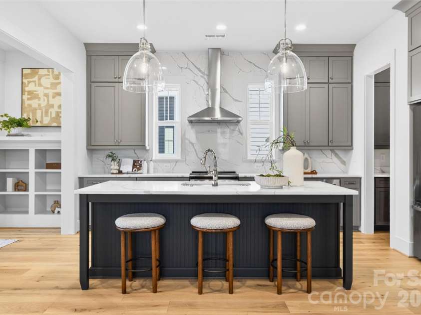 7245 Westrow Avenue, Charlotte, NC 28278.  MLS# CAR4314661, YatesRealty ID 982. Designer kitchen showcasing a spacious center island, stacked cabinetry extending to the ceiling for a custom-built look, and a sleek quartz backsplash that adds sophistication and easy maintenance.